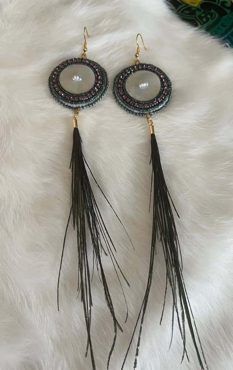 Beaded earrings with a mother of pearl centre in green and mauve, with long dark feather tassels